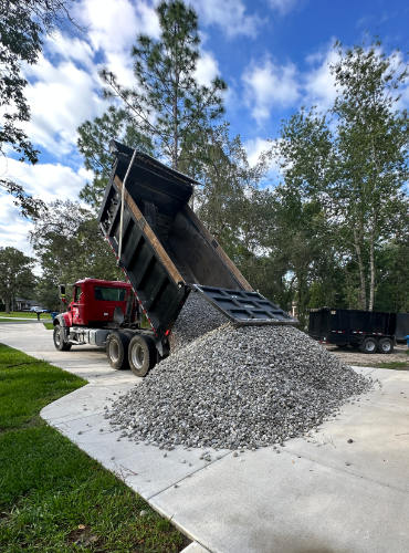 Wide shot of licensed inexpensive millings driveway delivery truck unloading into customer yard.